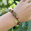 Red Jasper and Turquoise  beaded bracelet with a Buddha head and a large round logo on a model's wrist by Quantum Jewels. 